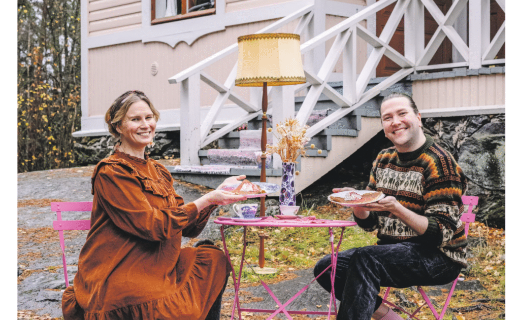 Kaksi henkilöä istuvat tuoleilla kalliolla, pitävät lettulautasia kädessä ja hymyilevät kameralle.