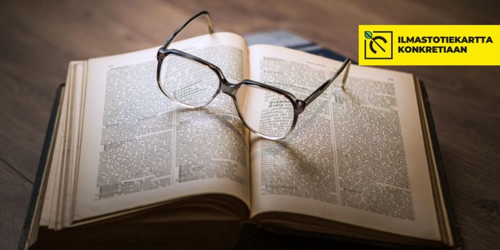 Puupöydällä avonainen kirja ja sen päällä silmälasit.