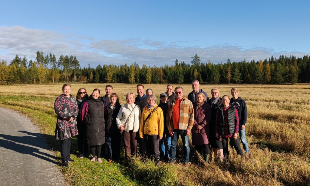 Henkilöitä ryhmäkuvassa pellonreunassa kauniissa syysilmassa.
